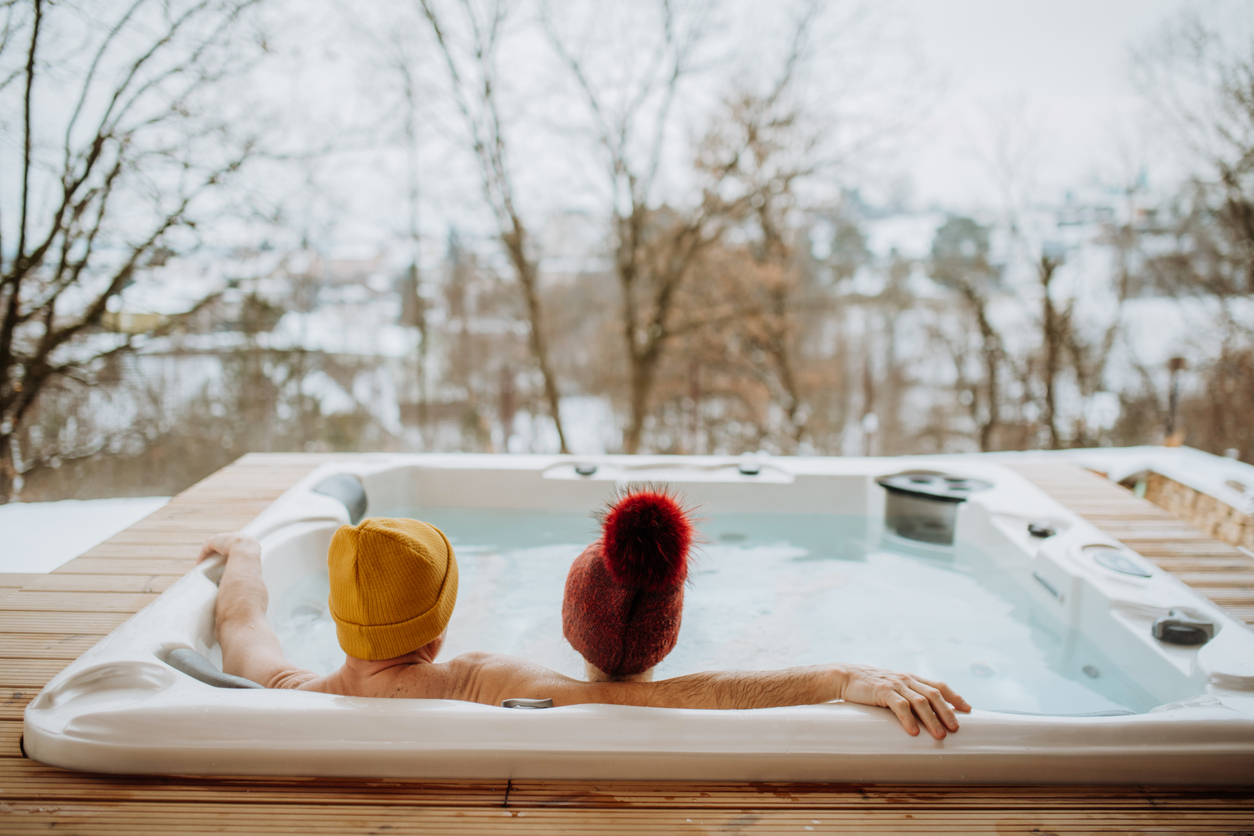 Senior couple in kintted cap enjoying together outdoor bathtub at their terrace during cold winter day. Electrician For Hot Tub Near Me